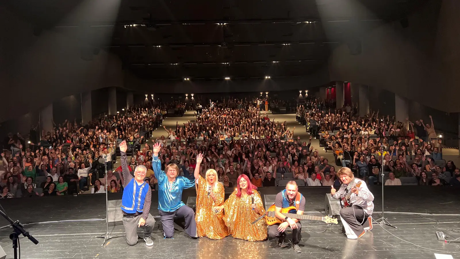 Banda no palco com o teatro lotado ao fundo, em Belo Horizonte